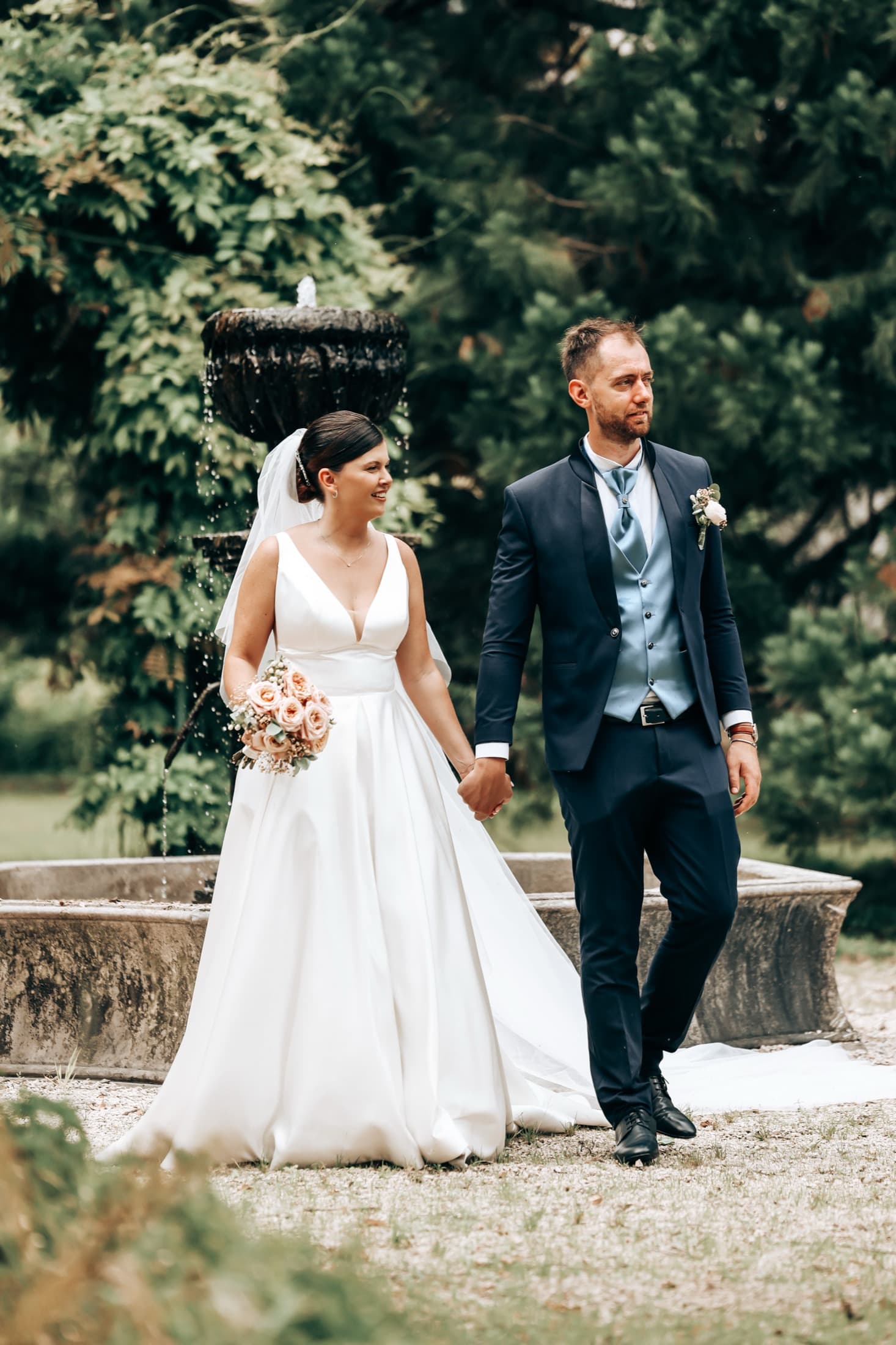 Newlyweds walking hand in hand past a garden fountain at an Italian estate